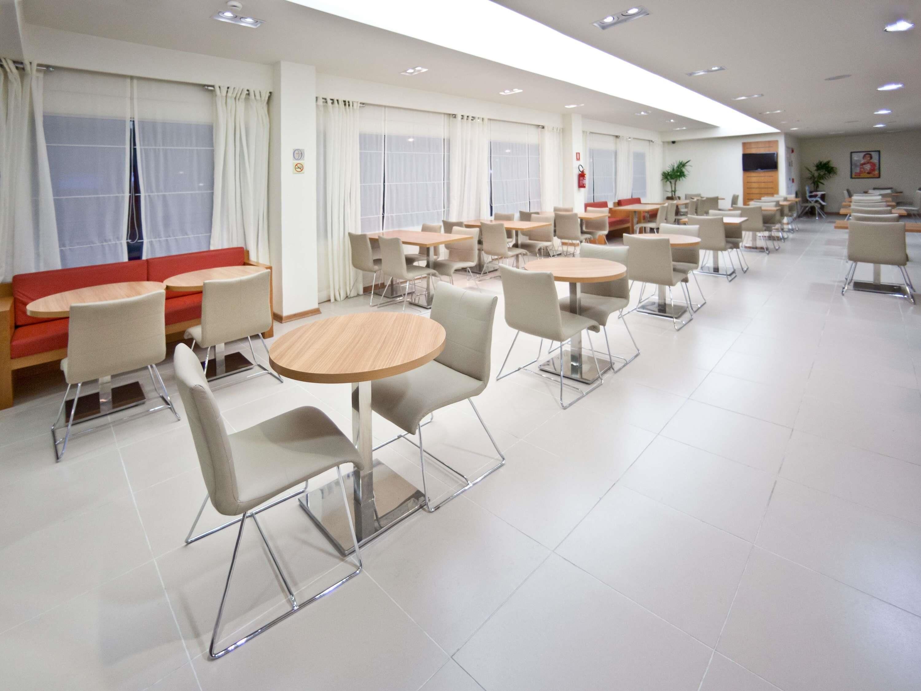 A modern dining area with round tables and chairs, a red sofa, and large windows with curtains.