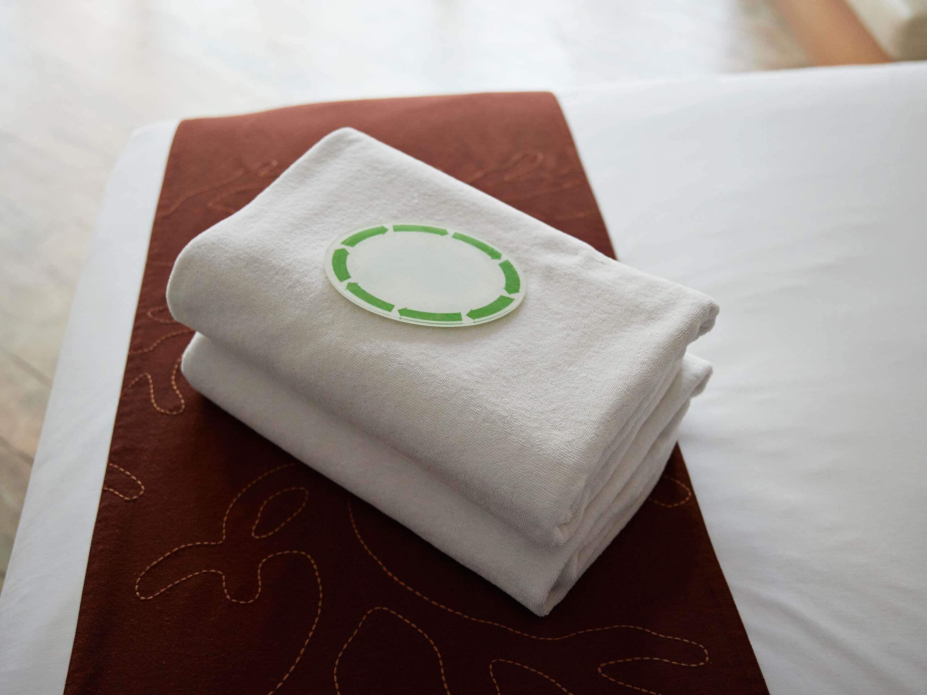 Een keurig opgevouwen witte handdoek met een groen cirkelvormig logo op een bruin kussen.