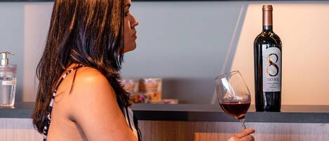 Una persona sosteniendo una copa de vino en un bar, con una botella que dice “RIO SOL” y varias otras botellas al fondo.