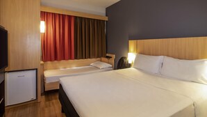 Una habitación de hotel con una cama grande, una cama más pequeña, un escritorio, una silla, un televisor y un refrigerador pequeño.