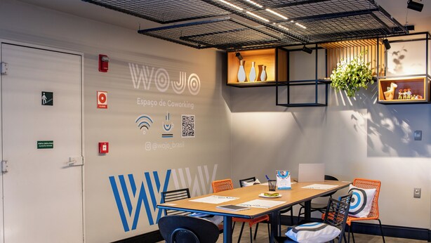 Un espacio de coworking moderno con un logotipo grande, una mesa de madera y varias sillas.