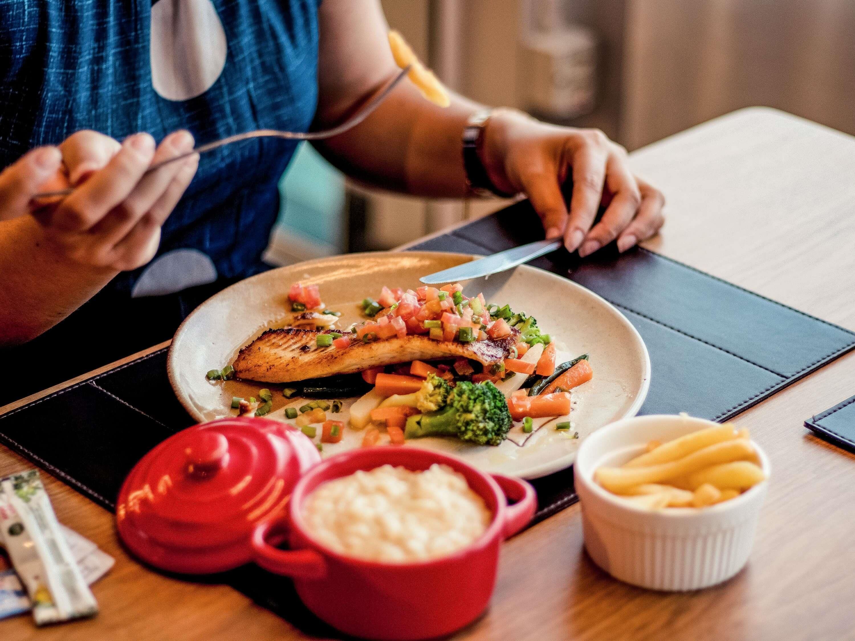 A dining table with a plate of food, a red pot, a white bowl, and a small container of fries.