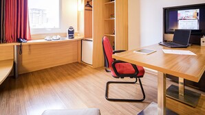 Un espacio de oficina moderno con un escritorio de madera, una silla de oficina roja, una computadora portátil y una televisión mostrando una interfaz de reserva de habitaciones.