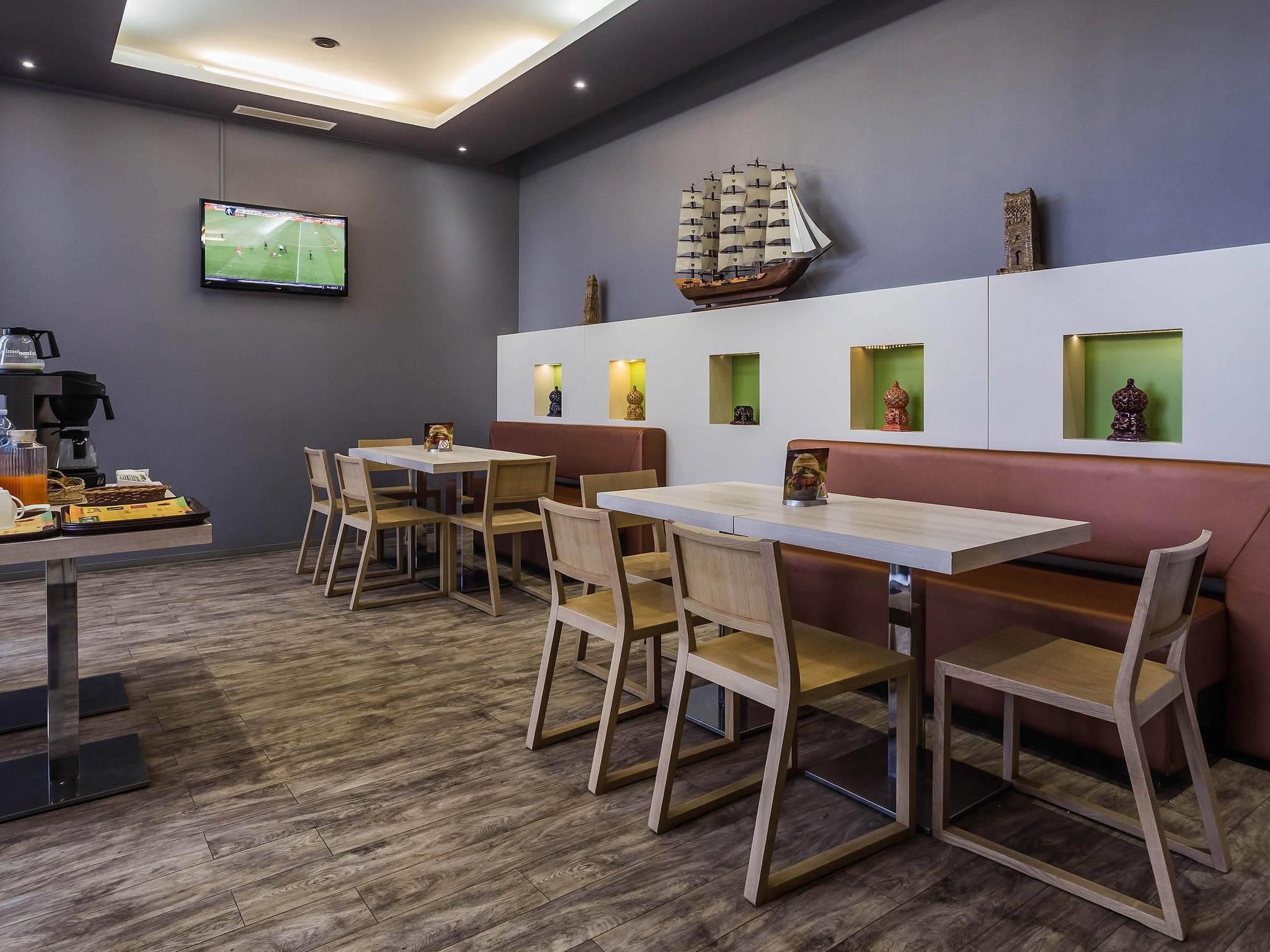 Un comedor moderno con mesas y sillas de madera, un televisor montado en la pared y exhibiciones decorativas de barcos y estatuas.
