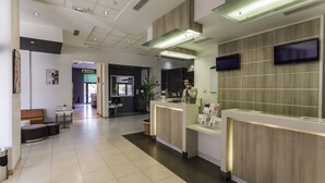 A modern reception area with a reception desk, a flat-screen TV, and a potted plant. - ibis Tlemcen (Tlemcen)