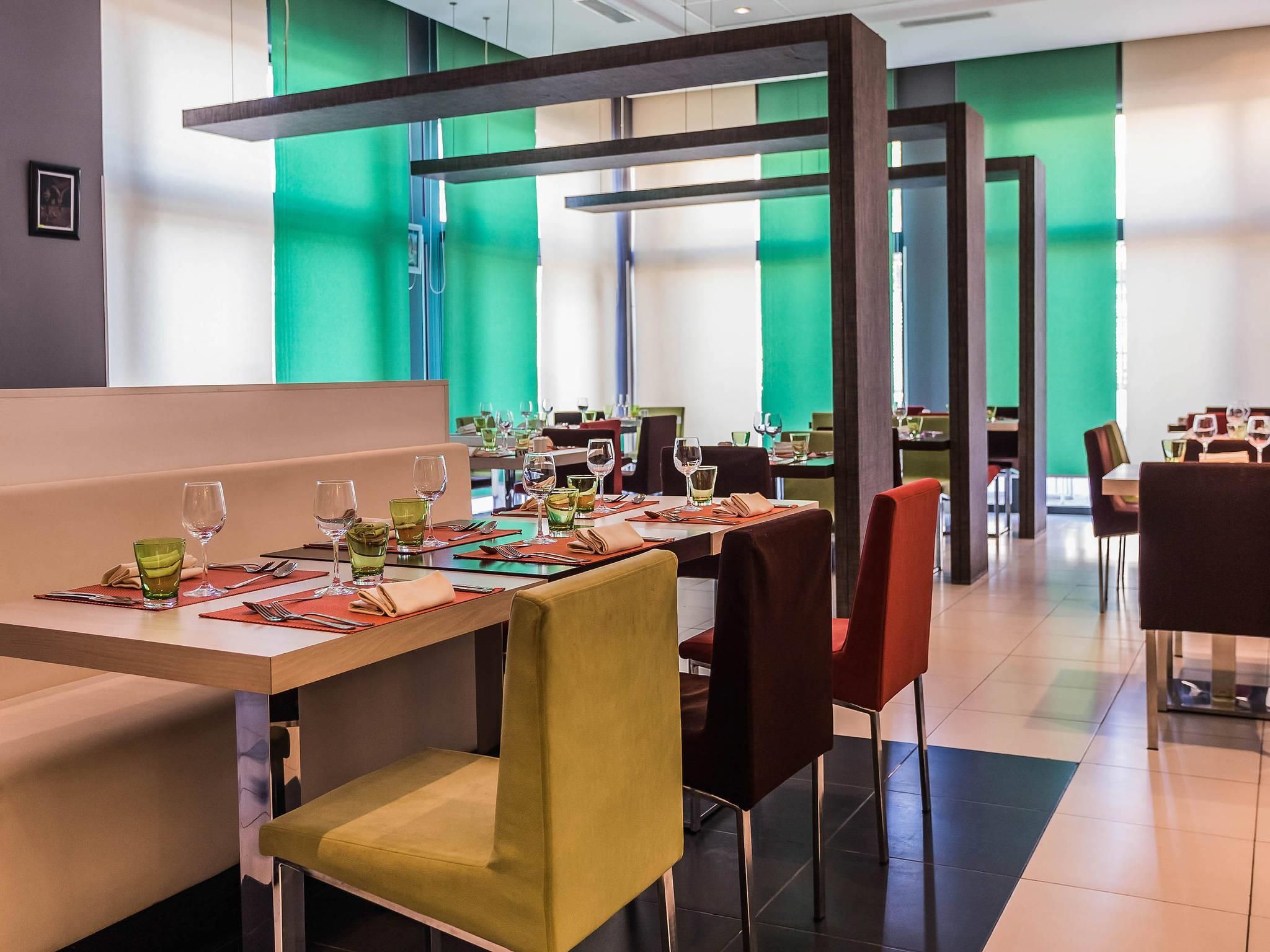 Un restaurant modern amb seients i taules, parets verdes i un disseny contemporani.