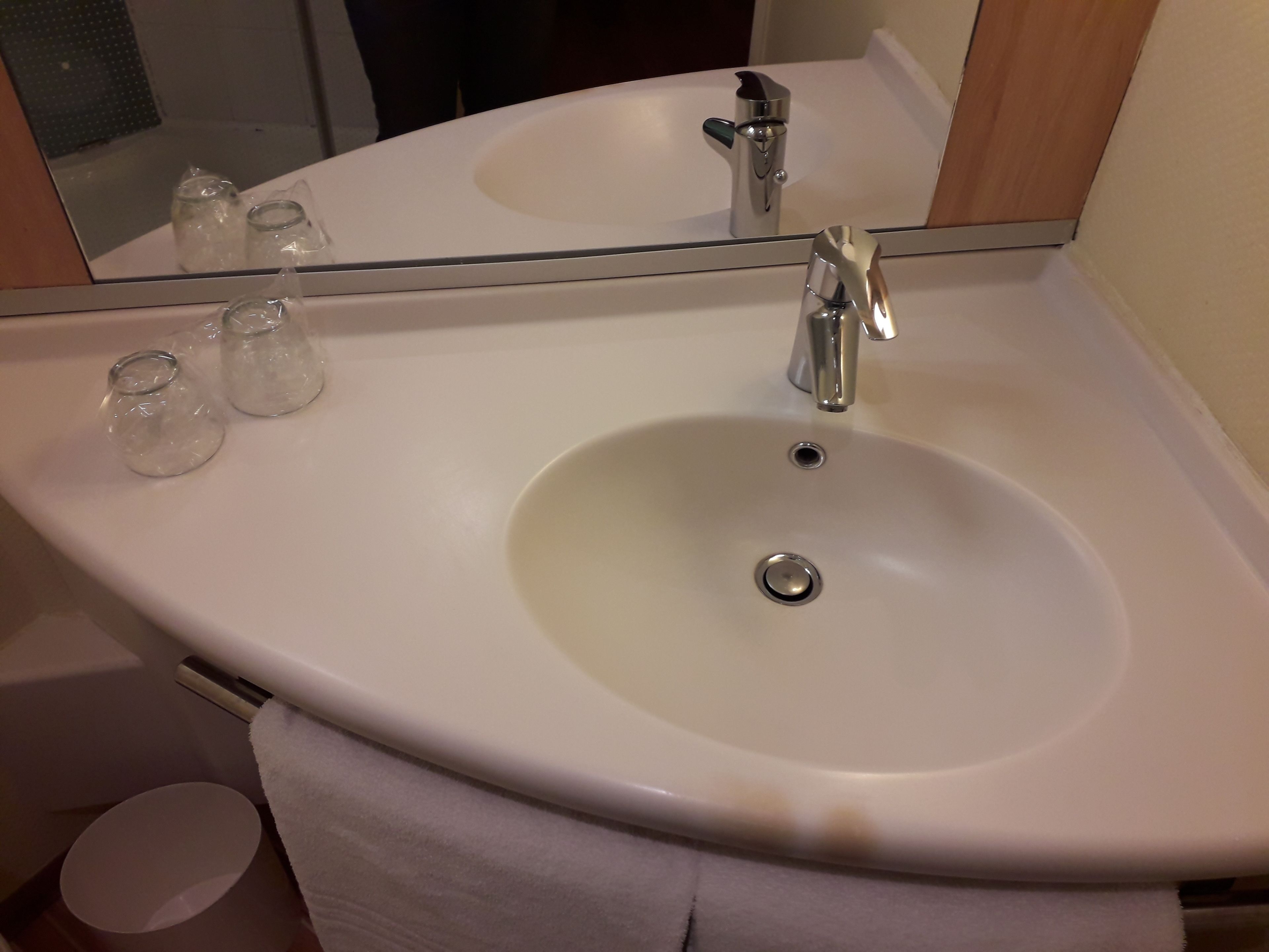Ein Badezimmerwaschbecken mit Spiegel darüber, einem Wasserhahn und zwei Glasbehältern auf dem Waschbecken.