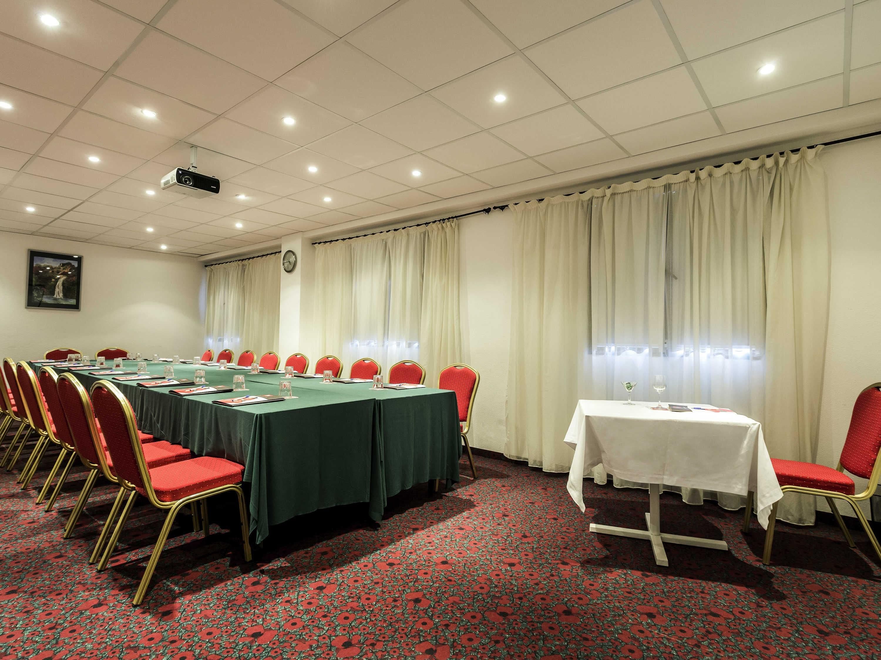 A conference room with a long table, red chairs, a white table with a white tablecloth, and a red carpet with a floral pattern.