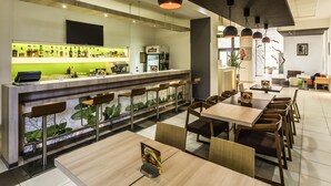 Un restaurant moderne doté d’un bar, de différents espaces pour s’asseoir et d’un mur végétal.