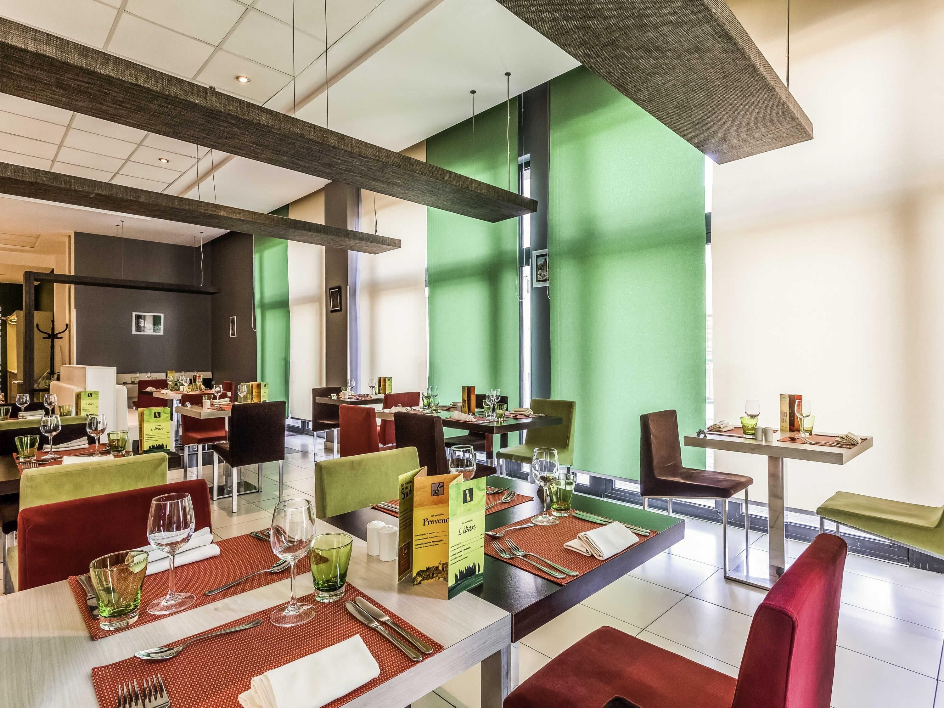 Un restaurante moderno con varias mesas, sillas rojas y verdes, y una pared de acento verde.