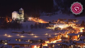 A snow-covered village with illuminated buildings and a castle-like structure in the background. - Vötter's Hotel (Kaprun)