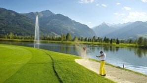 Un campo da golf con un lago, una fontana e montagne sullo sfondo.