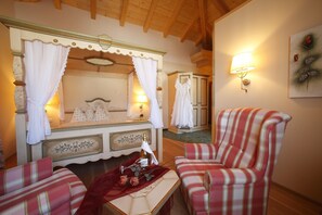 A cozy room with a bed, a chair, a table with a bottle and flowers, and a wall-mounted lamp. - Vötter's Hotel (Kaprun)