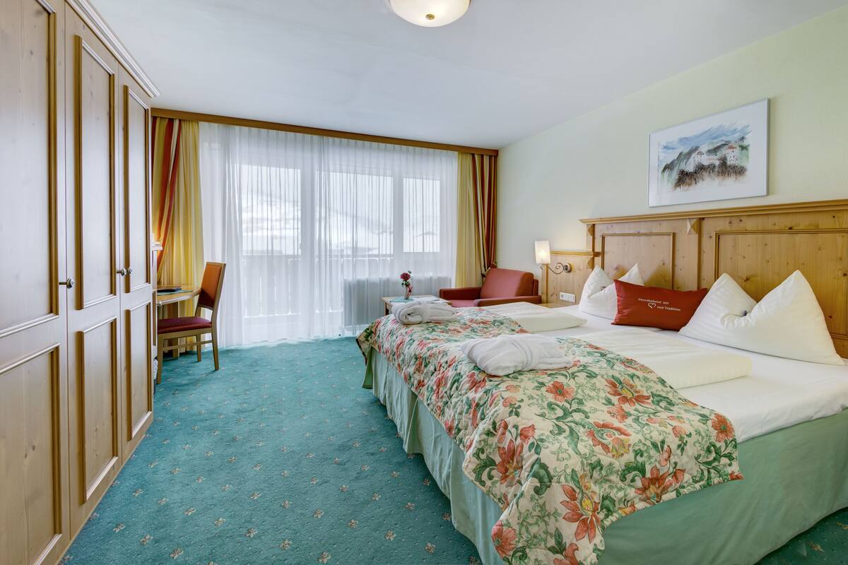 A hotel room with a bed, a desk, a chair, and a window with curtains.