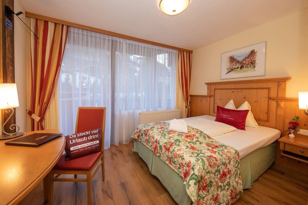 A hotel room with a bed, a desk, a chair, and a window with curtains.