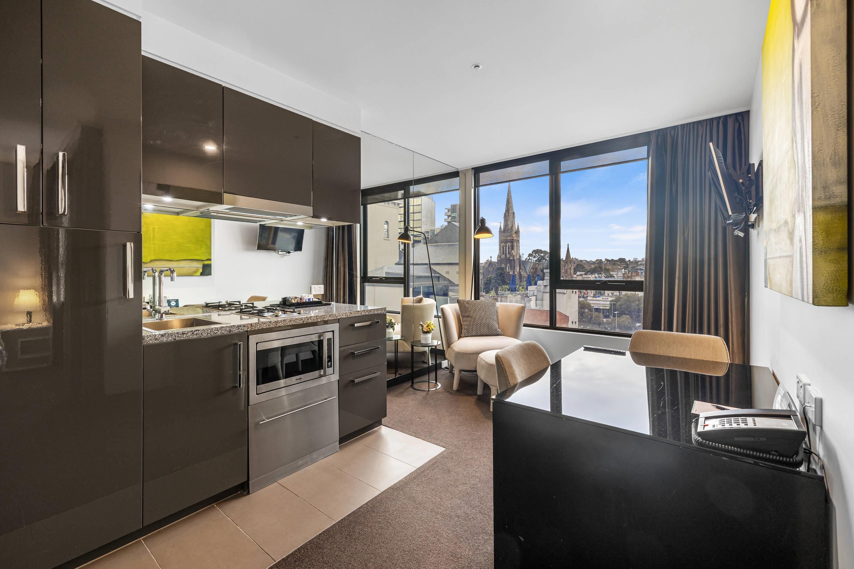 Une cuisine moderne équipée d’appareils électroménagers en acier inoxydable, un coin repas offrant une vue sur les toits de la ville, et une grande fenêtre agrémentée de rideaux.