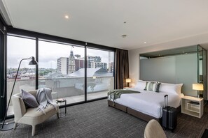 Una habitación de hotel con un ventanal grande, una cama, una silla, un escritorio y una maleta.