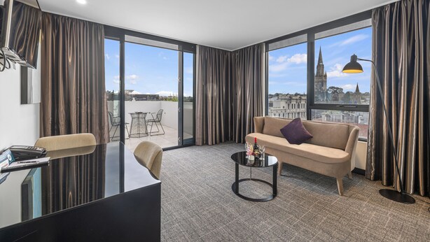 Ein modernes Hotelzimmer mit einer Couch, einem Couchtisch, einem Schreibtisch und großen Fenstern mit Blick auf die Stadt.