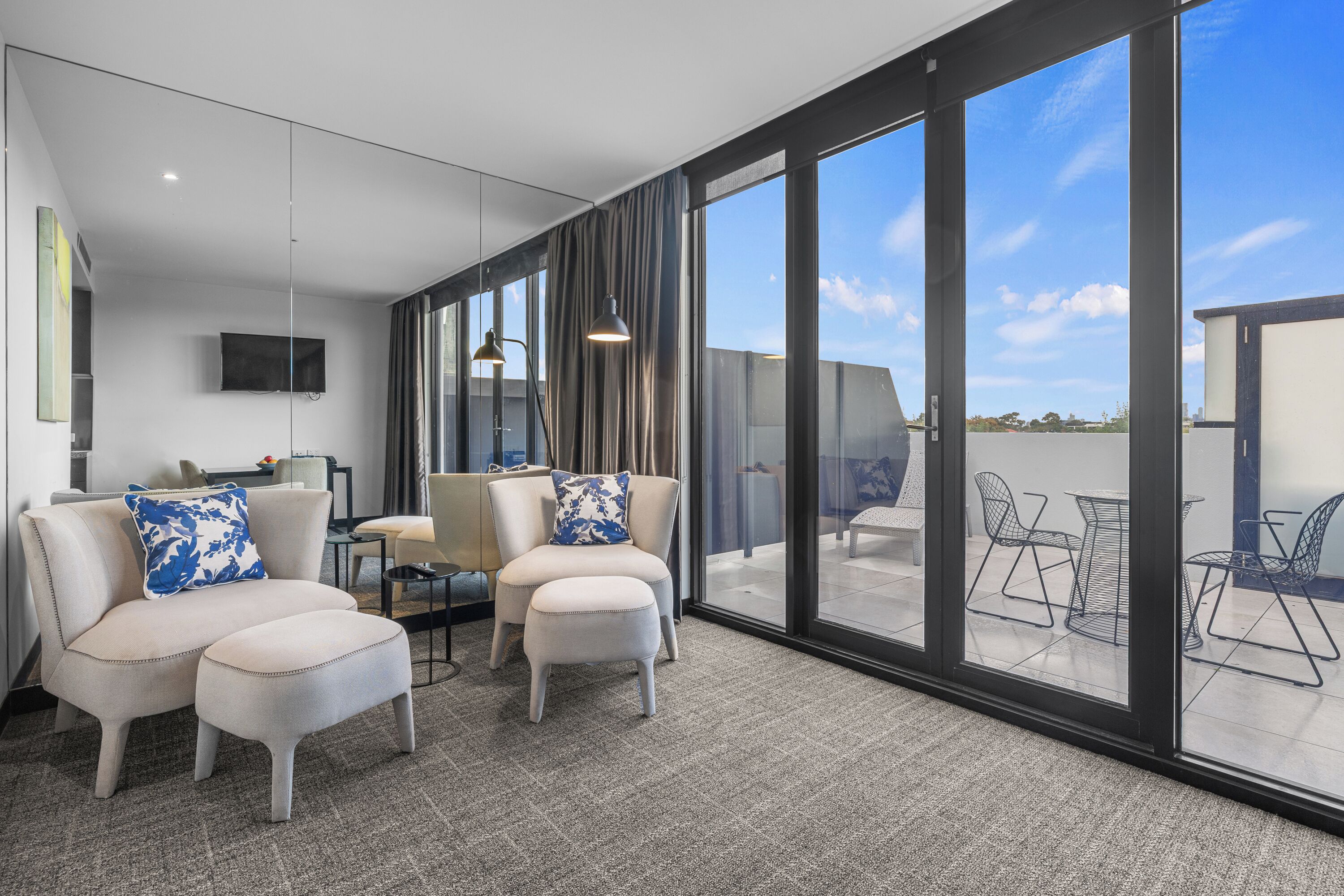 A modern interior with a sofa set, a flat-screen TV, and a view through large glass doors to an outdoor seating area.