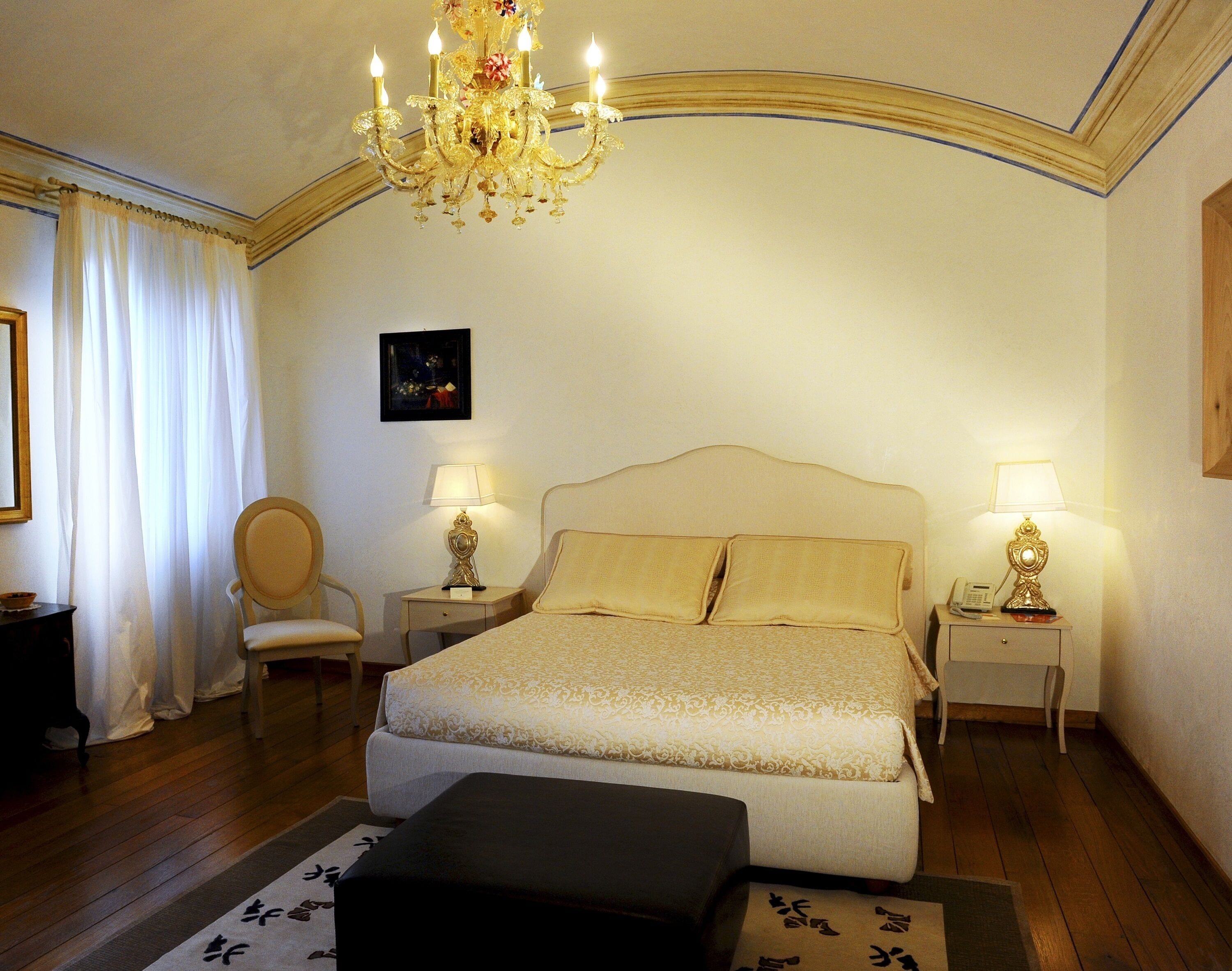 Une chambre d’hôtel avec un grand lit, deux lampes de chevet, une chaise, un bureau et un lustre.
