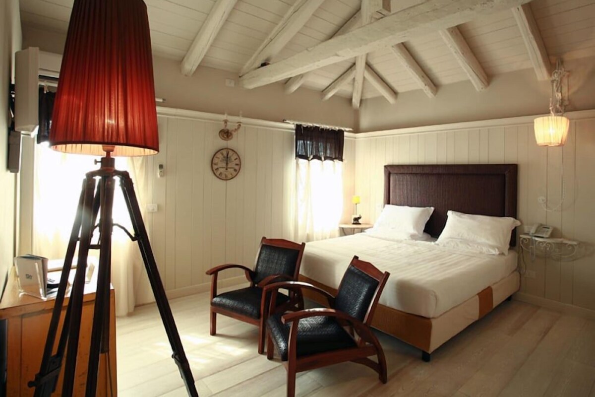 Une chambre à coucher avec un lit, deux chaises, une lampe, une horloge et une fenêtre avec des rideaux.
