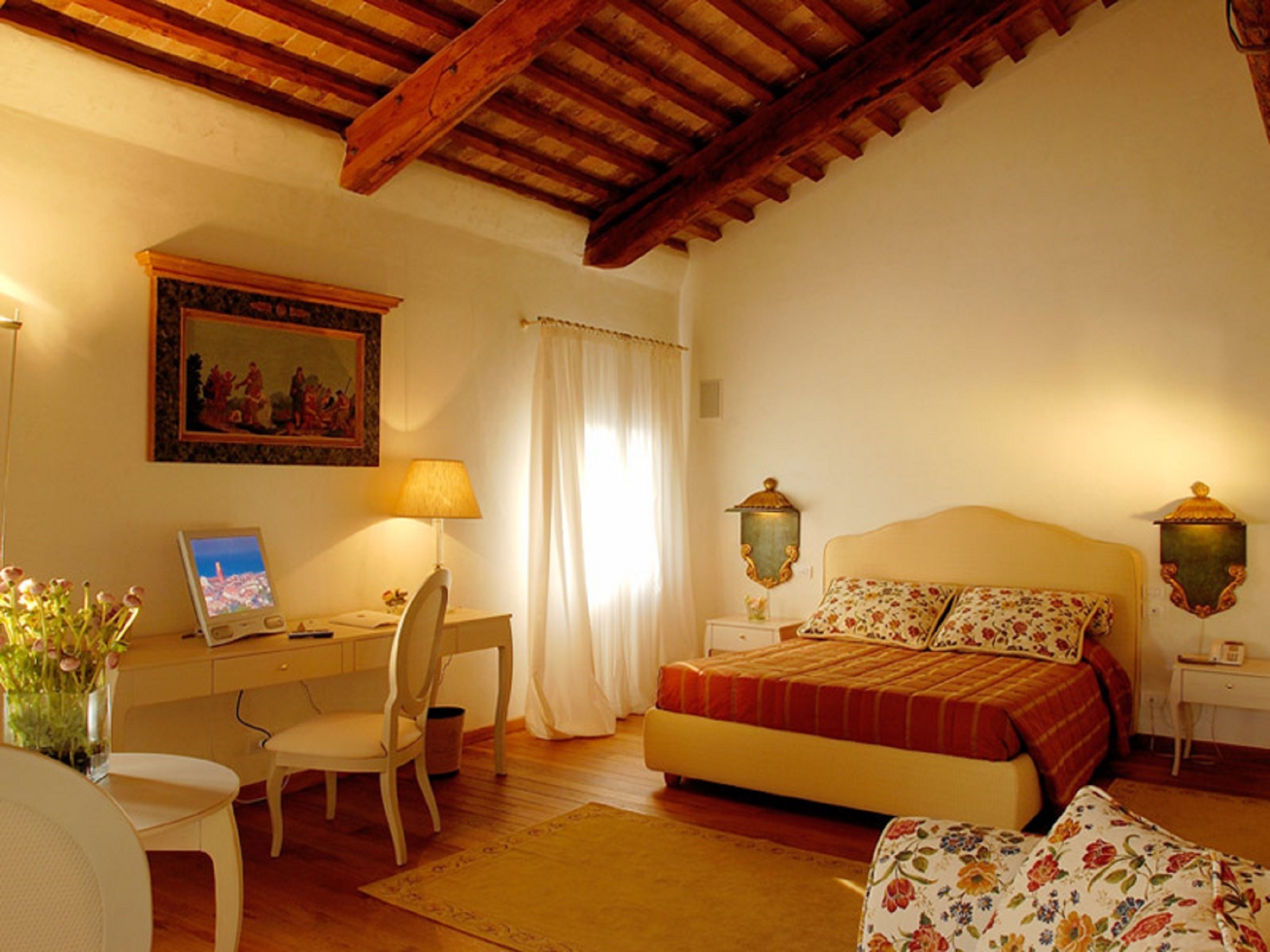 A bedroom with a bed, a desk with a chair, a lamp, a painting, and a nightstand with a lamp.