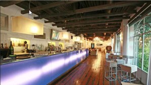 Een bar met een lange toonbank, houten vloeren en uitzicht op de omgeving door grote ramen.