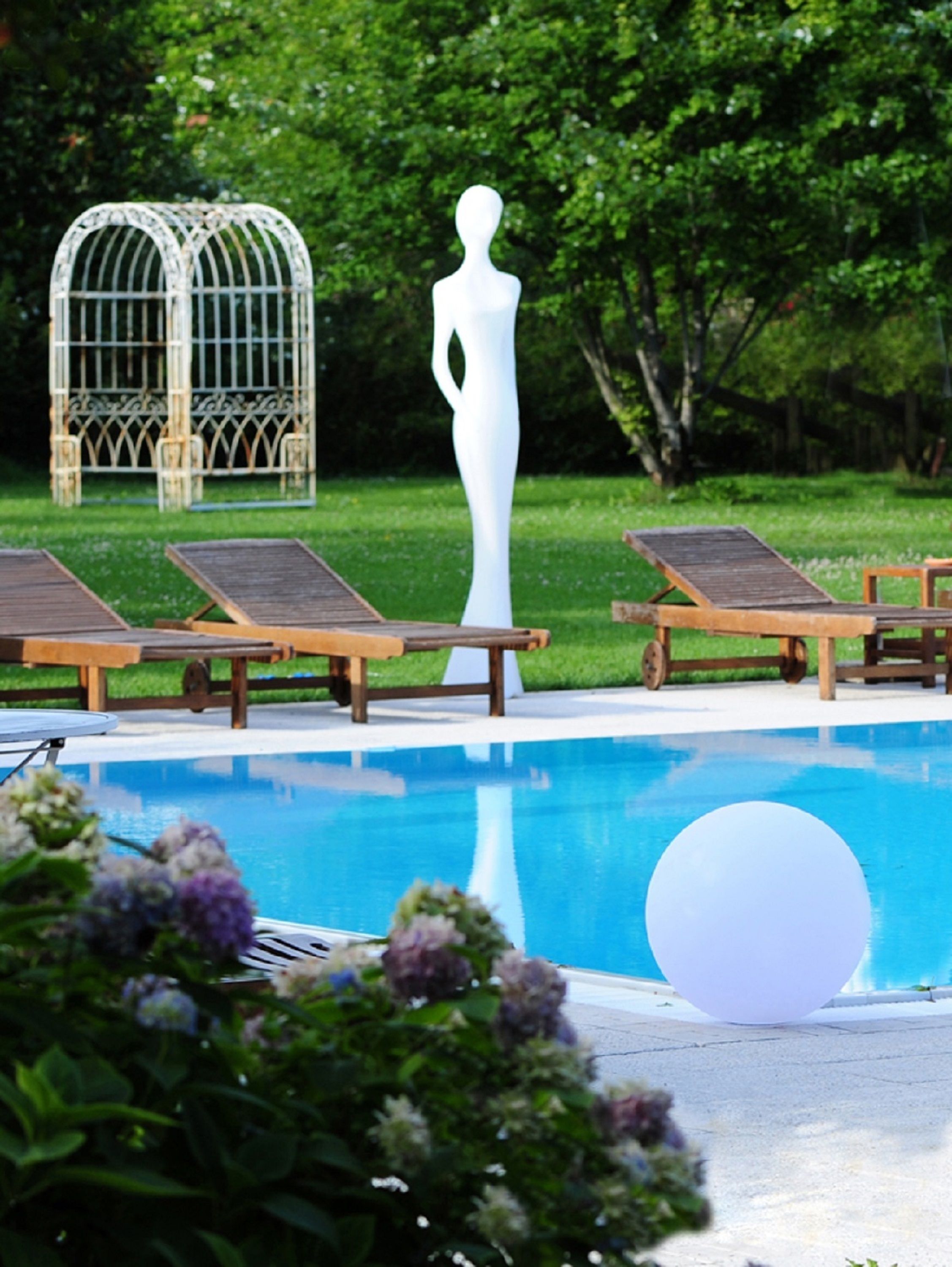 Un espace piscine avec des chaises longues, une statue blanche et une cage à oiseaux.