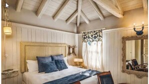 Een slaapkamer met een groot bed, een houten hoofdbord, twee nachtkastjes, een spiegel en een raam met gordijnen met een patroon.