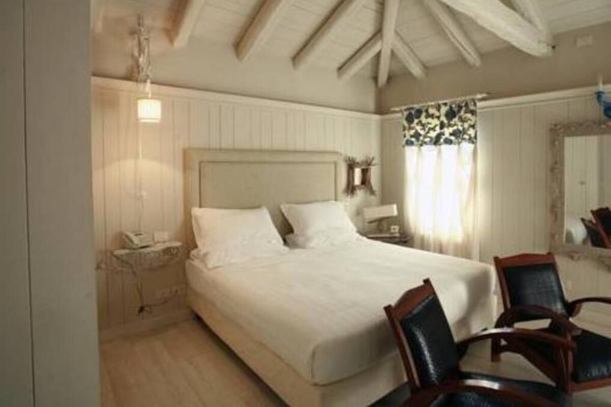 Ein Schlafzimmer mit einem großen Bett, einem Holz-Kopfteil, einem Nachttisch, einem Sessel und einem Fenster mit Vorhängen.