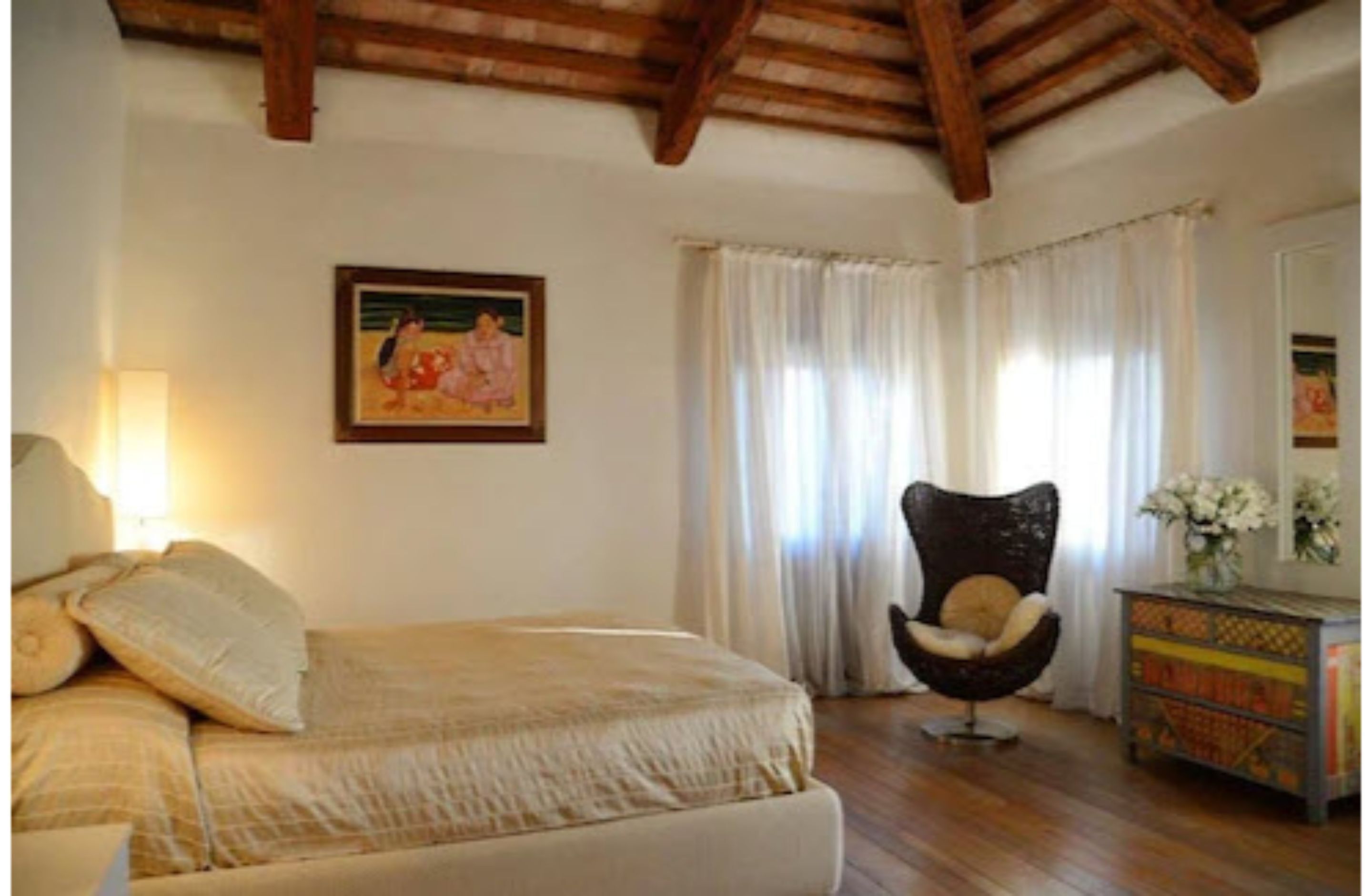 Une chambre à coucher avec un lit, une chaise, une commode et un tableau accroché au mur.