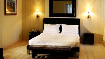 A large bed with a wooden frame, two bedside tables, a nightstand, and a wall-mounted mirror.