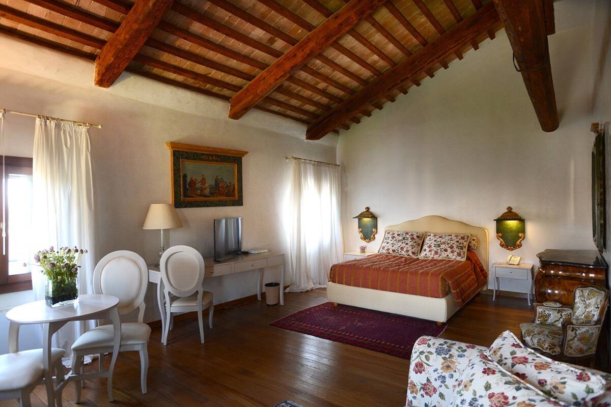 Ein Schlafzimmer mit einem Bett, einem Schreibtisch, einem Sessel, einem Fernseher und einem Bild an der Wand.