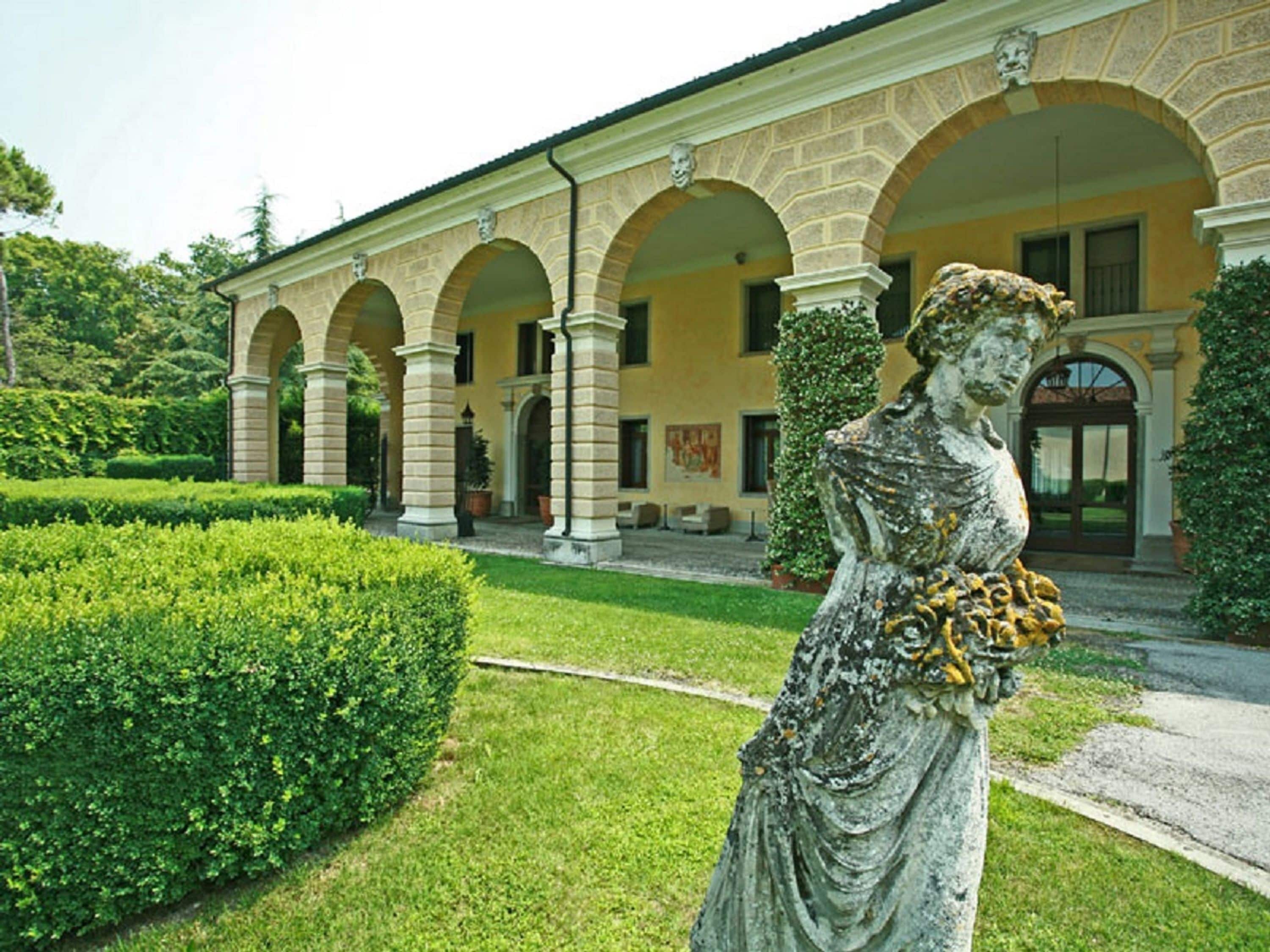 Ein klassizistisches Gebäude mit einer zentralen Statue in einem gepflegten Garten.