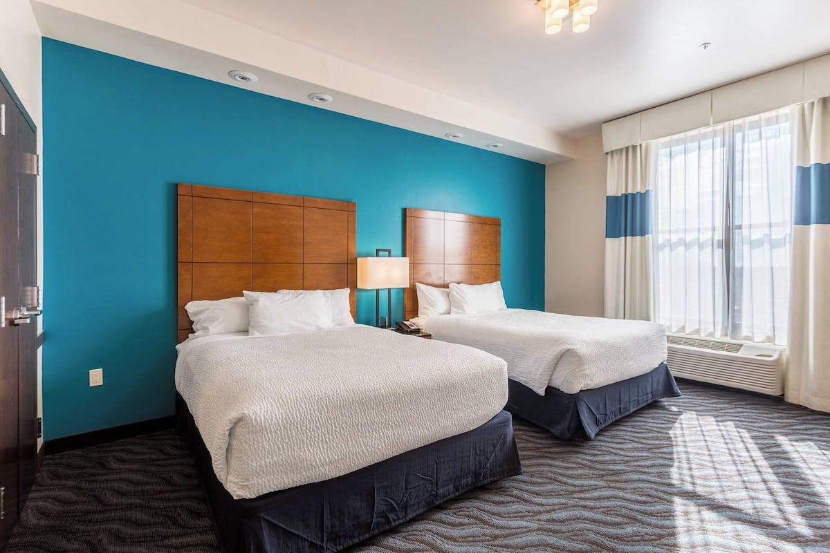 A hotel room with two beds, a blue accent wall, a patterned carpet, and a large window with curtains.