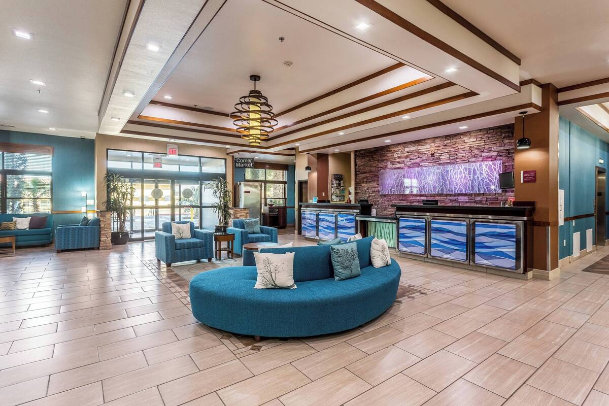 A spacious lobby with a curved blue sofa, a stone wall with a TV, and a corner market sign.