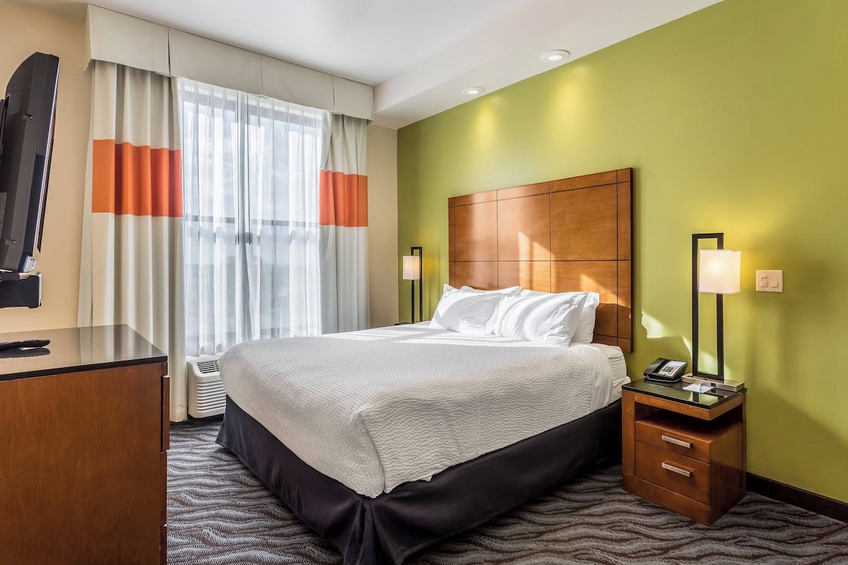 A hotel room with a bed, a desk, a chair, a TV, and a nightstand with a lamp.