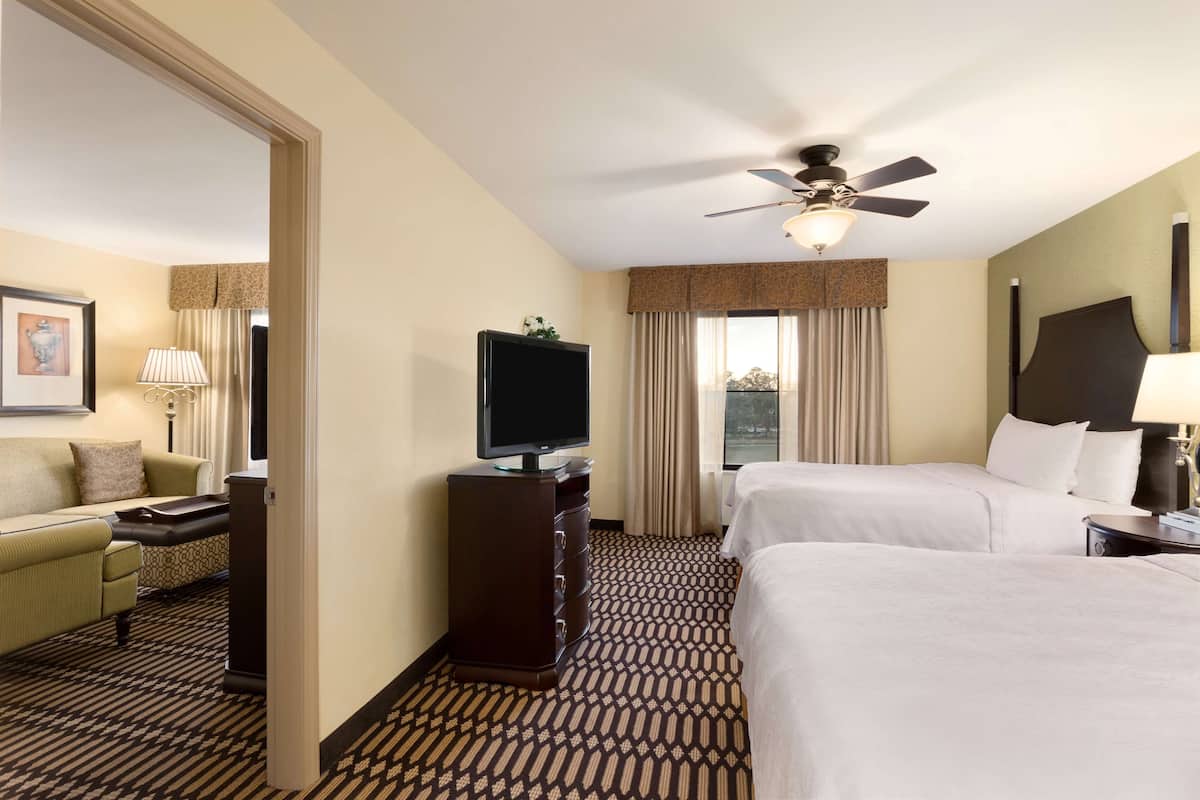 Habitación de hotel con dos camas, un televisor, un escritorio y un ventilador de techo.