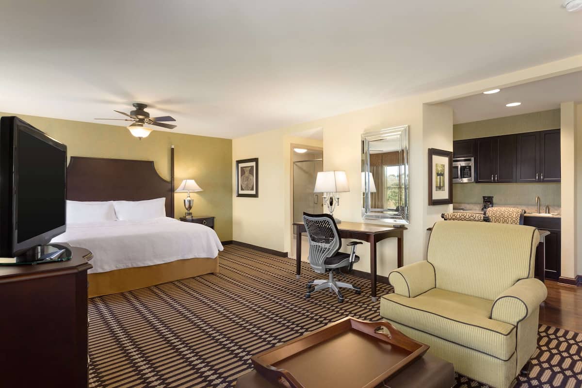 Habitación de hotel con cama, escritorio, silla, televisor y kitchenette.