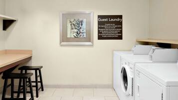 A laundry area with a sign detailing guest laundry rules, a framed artwork, and a seating area with stools.
