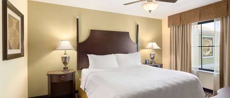 A hotel room with a large bed, two bedside tables with lamps, a ceiling fan, and a window with curtains.