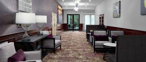 A hotel lobby with a patterned carpet, seating areas with cushions, a chandelier, and artwork on the walls.