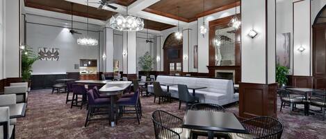 Un amplio vestíbulo de hotel con techos altos, un área de estar central y un bar.