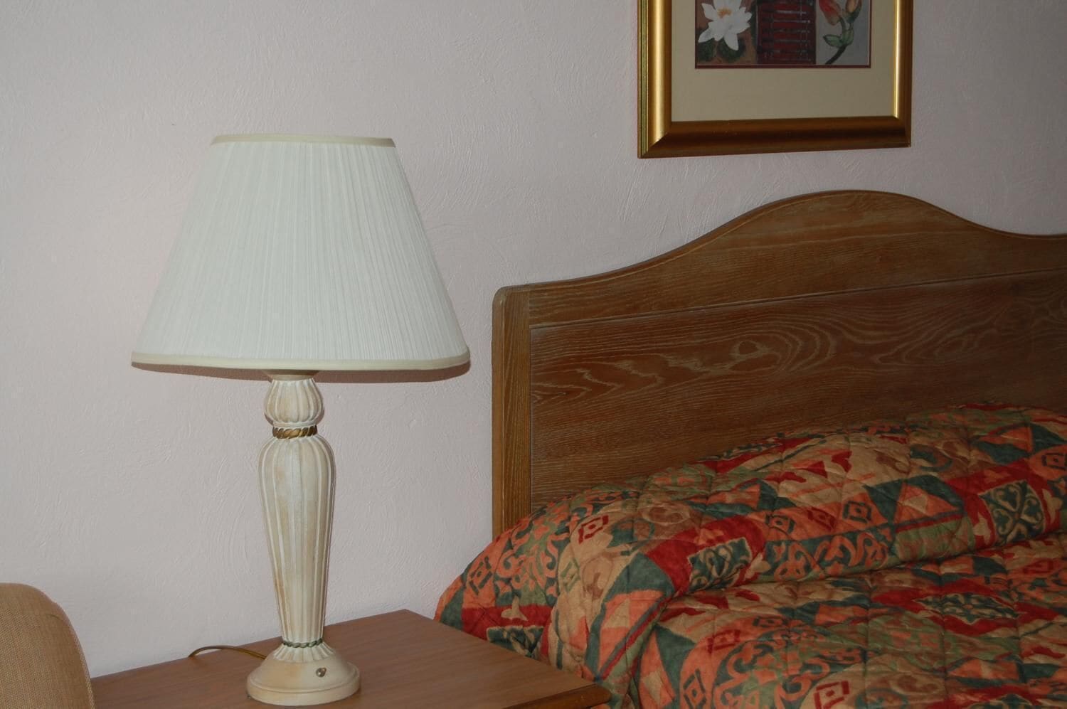 Una habitación con cabecera de madera, colcha estampada y lámpara de mesa blanca.