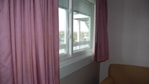 A room with a window, a brown sofa, and pink curtains. - Sea Breeze Inn (Ocean City)