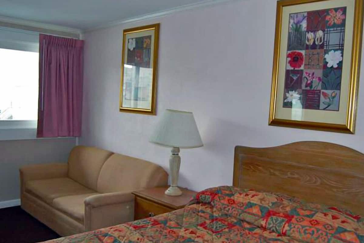 Habitació d'hotel amb un llit, un sofà, una cambrera amb una làmpada i dues fotografies emmarcades a la paret.