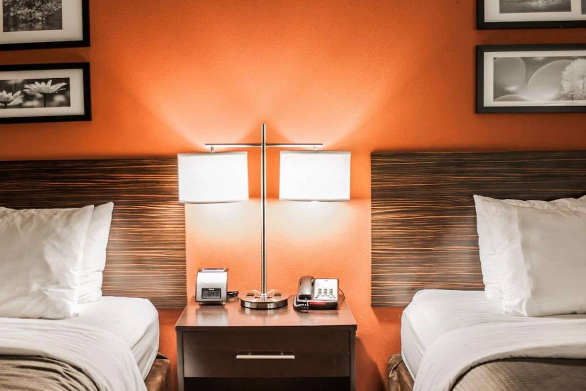 Una habitación de hotel con dos camas, una mesita de noche con lámpara, un reloj y un teléfono.