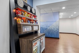 Exhibición de aperitivos con diversos alimentos envasados, un refrigerador de bebidas y un mural en la pared.