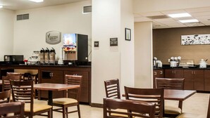 A dining area with wooden tables and chairs, a coffee machine, and a refrigerator.