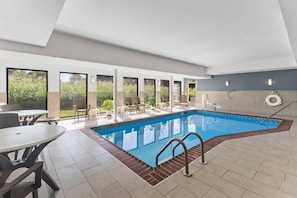 A modern indoor swimming pool with clear glass walls, a tiled floor, and a poolside seating area with chairs and tables. - Sleep Inn & Suites Fort Campbell (Oak Grove)